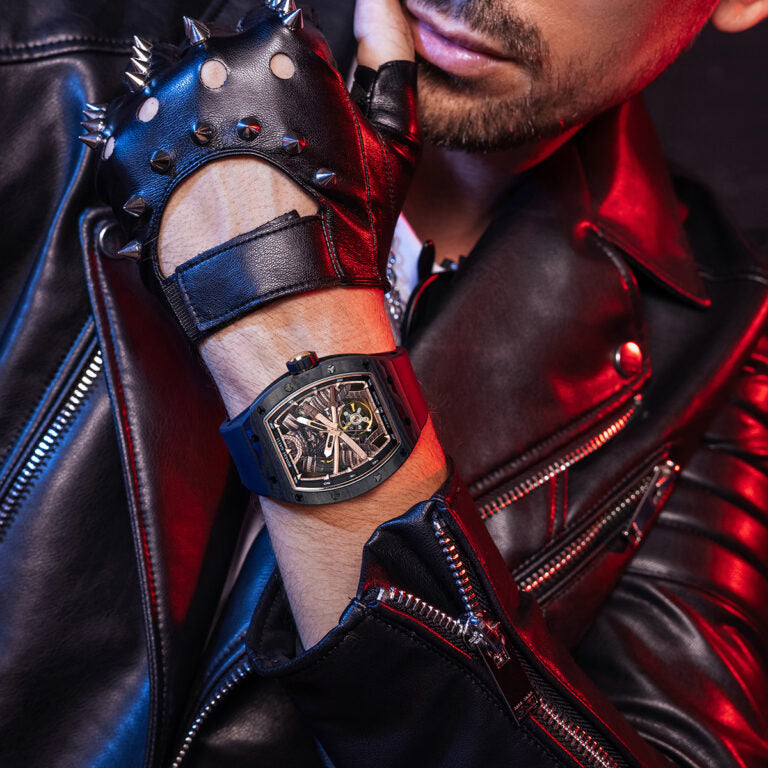 Person wearing a black leather glove with spikes and a red and black jacket, showcasing a detailed wristwatch.