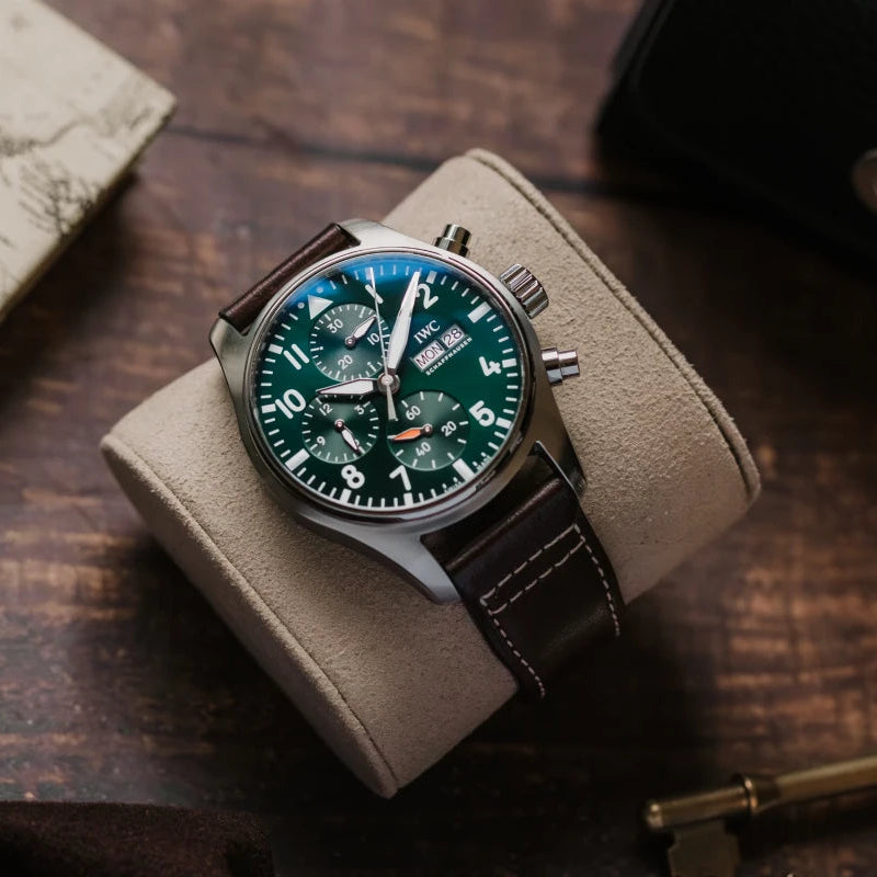 Wristwatch with green dial and brown leather strap on a wooden surface with keys and map.