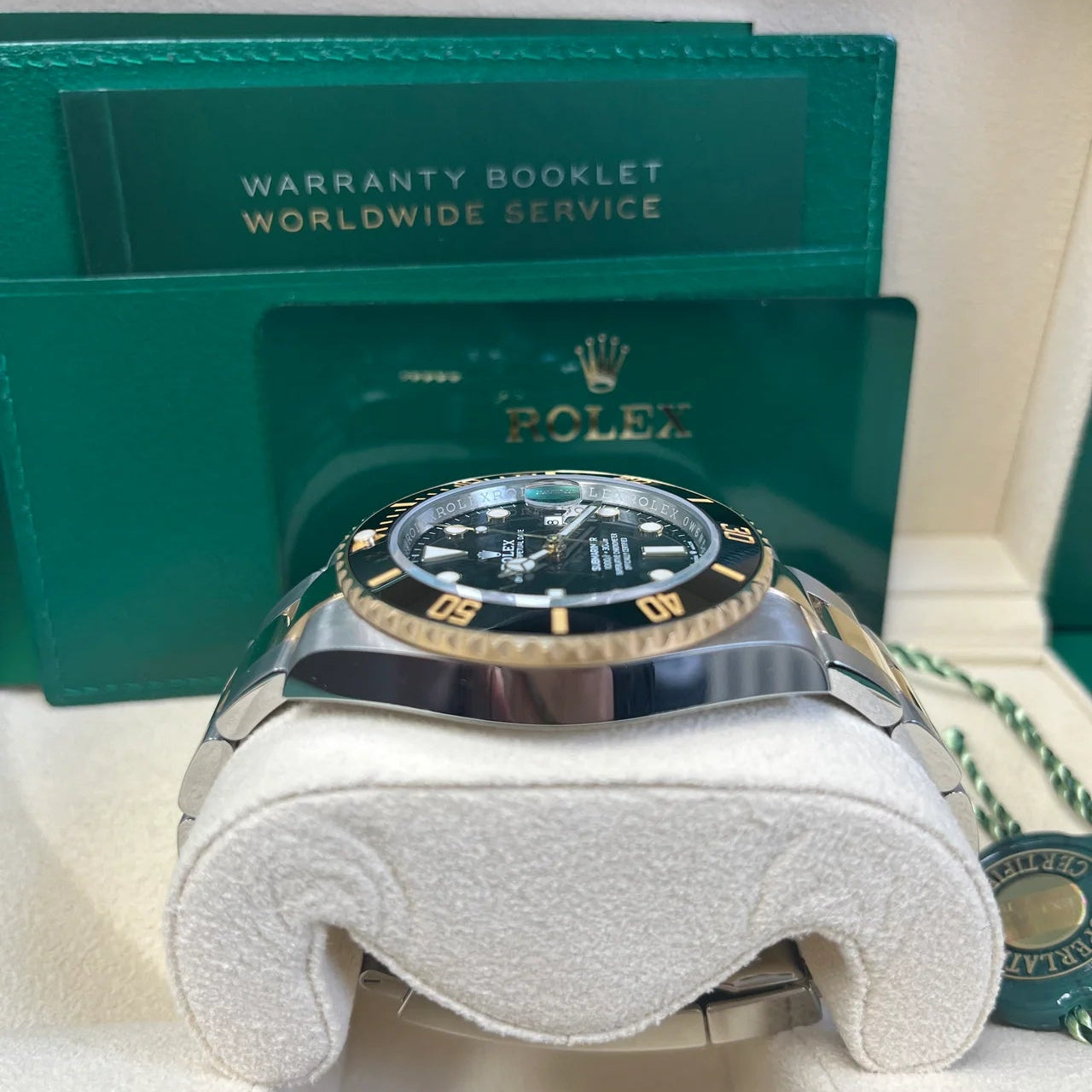 Rolex watch with green warranty booklet on a white surface
