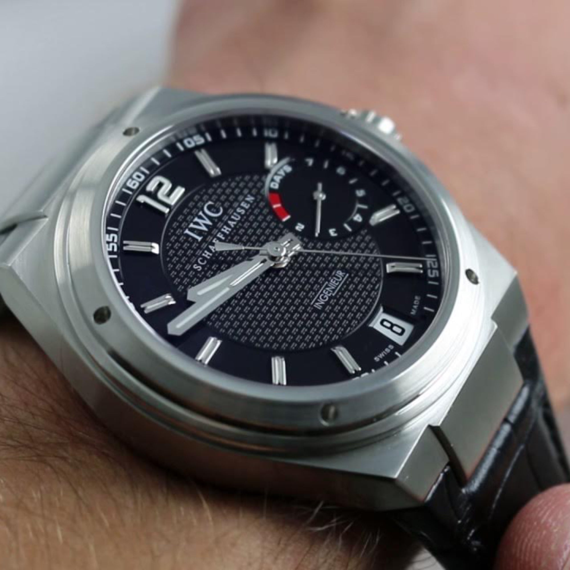 Close-up of a wrist wearing a silver IWC watch with a black face.