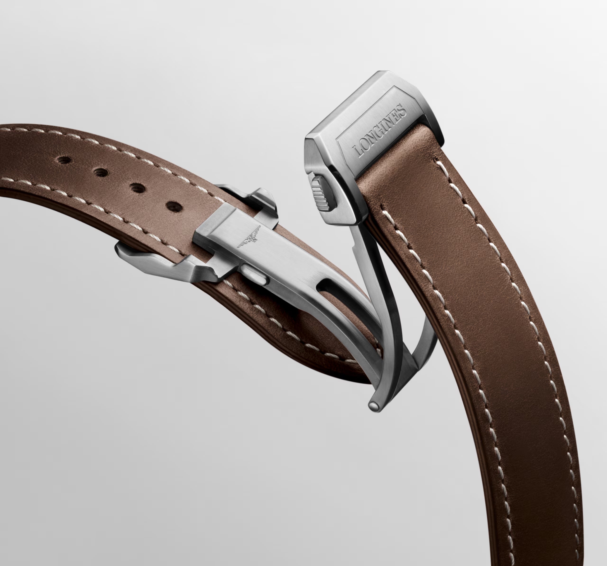 Close-up of a brown leather watch strap with silver clasp on a light gray background
