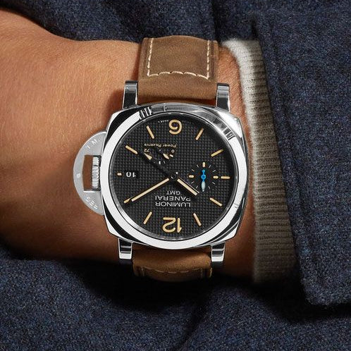 Watch with brown leather strap on a wrist, wearing a dark suit jacket.