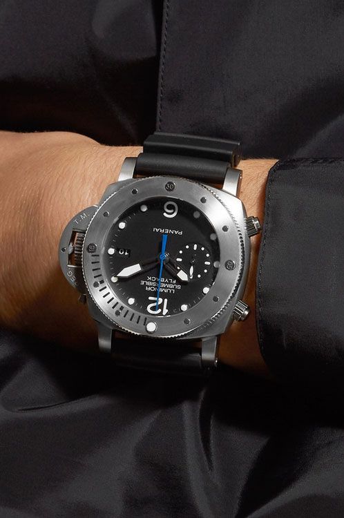 Black wristwatch with detailed face on a person's wrist against a dark background