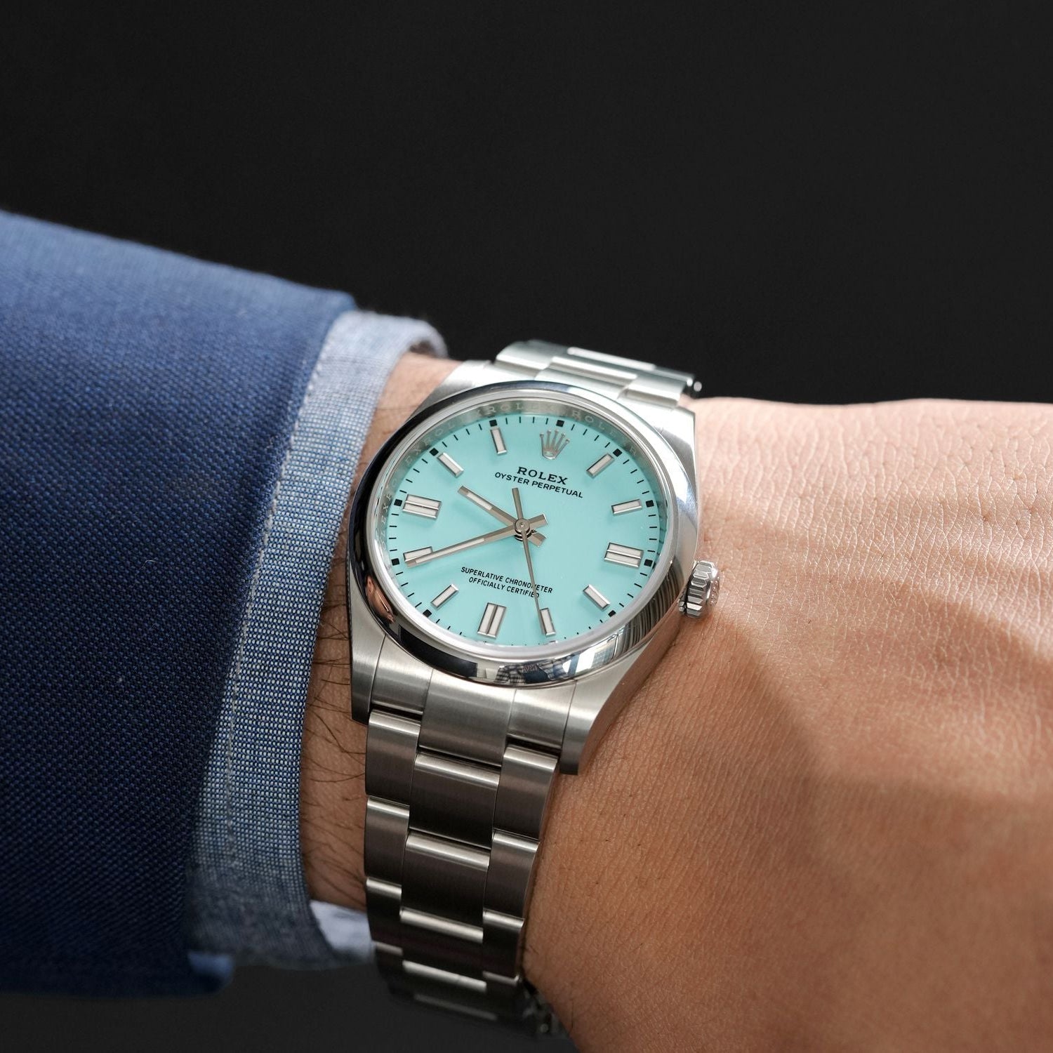Silver Rolex watch with a light blue face on a wrist against a dark background