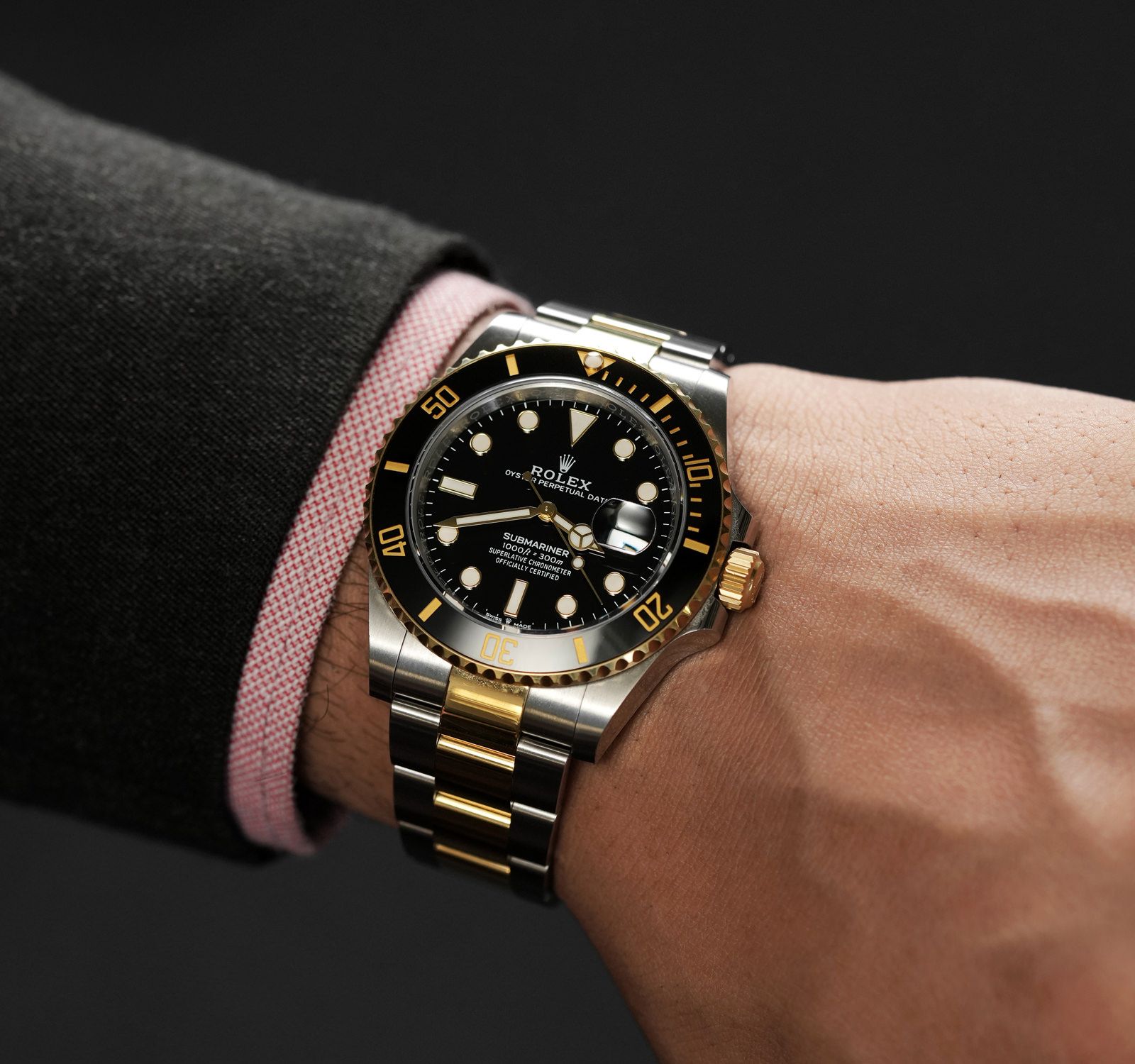 Luxury watch with black dial and gold accents on a wrist against a dark background