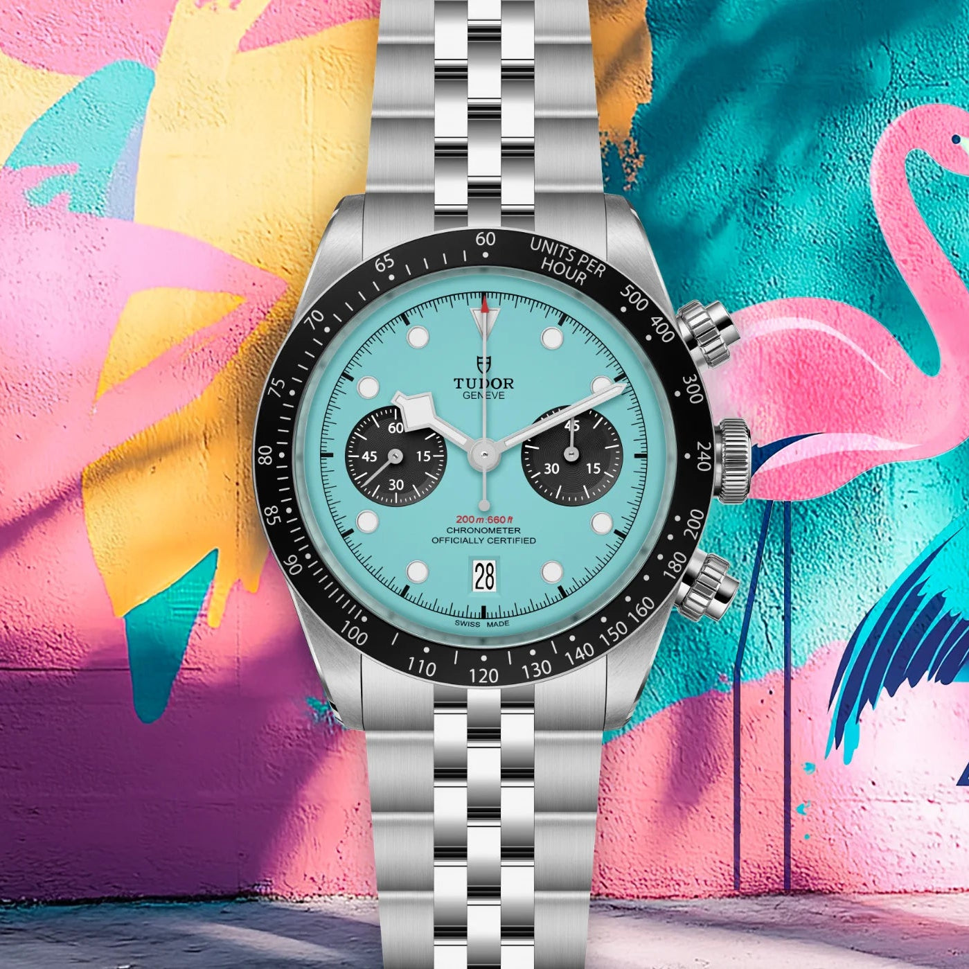 Silver watch with a turquoise face against a colorful flamingo mural.