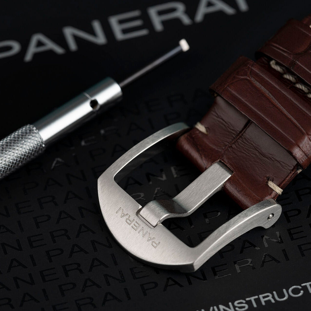 Brown watch strap with silver buckle on a Panerai branded surface