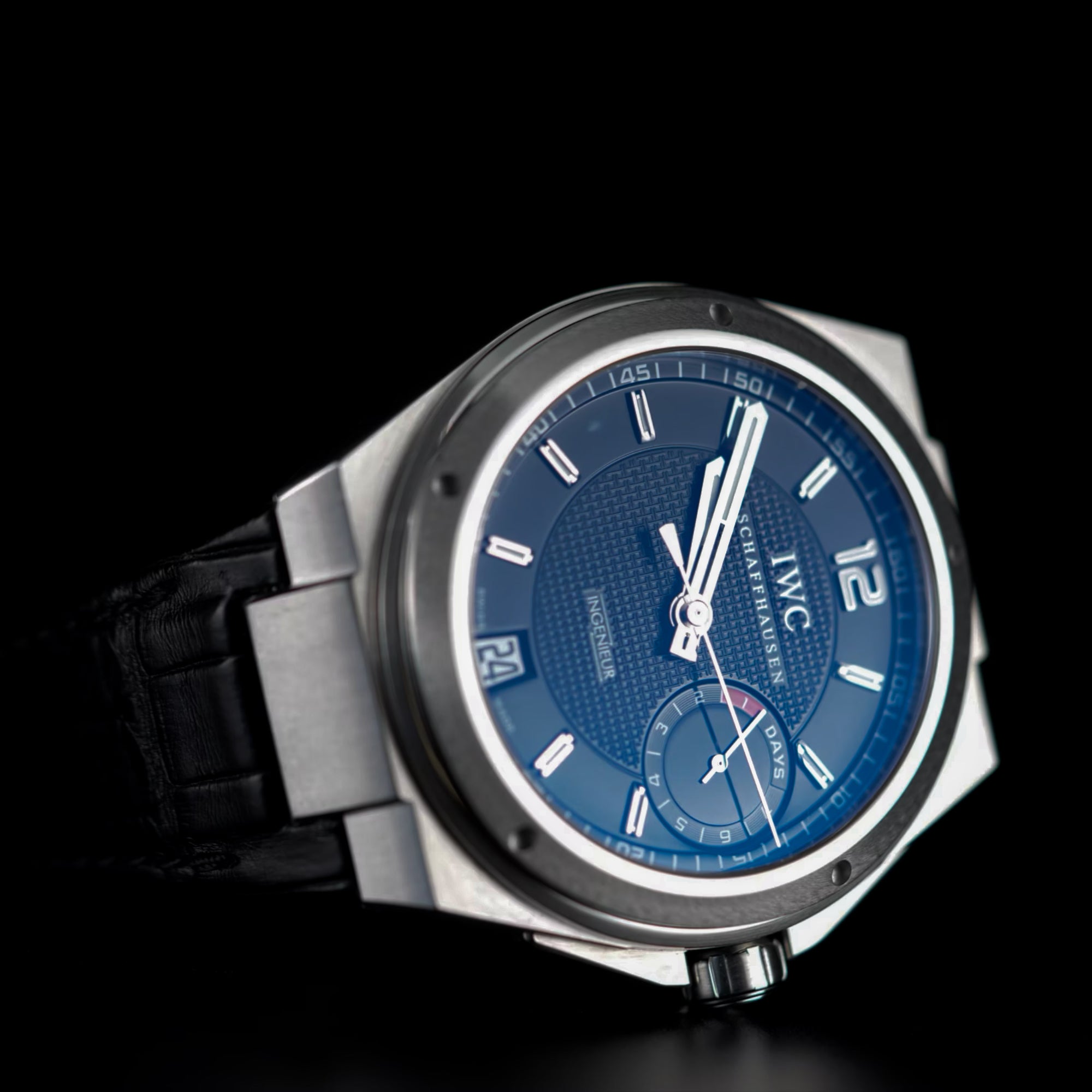 IWC watch with blue dial and black strap on a dark background