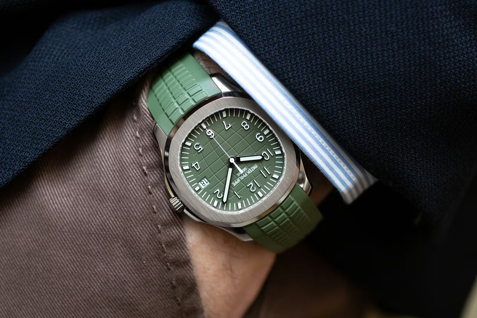 Green watch with a green strap worn on a wrist, partially tucked into a dark shirt pocket.