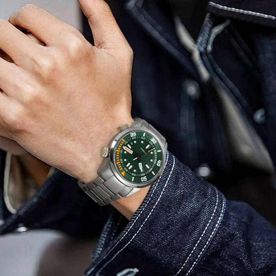 Hand wearing a silver watch with a green face, close-up shot.
